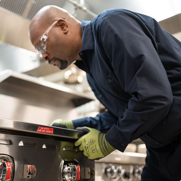 Technician in work gloves inspecting the controls of a commercial range