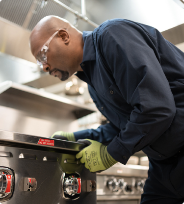 Technician in work gloves inspecting the controls of a commercial range