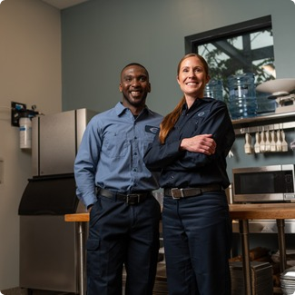 Two A-1 Services Group technicians, a man and a woman, smiling in a commercial kitchen