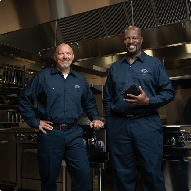Two uniformed A-1 Services Group technicians standing side by side in a restaurant kitchen