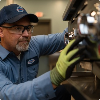 A-1 Services Group technician in safety glasses and work gloves repairing commercial kitchen equipment