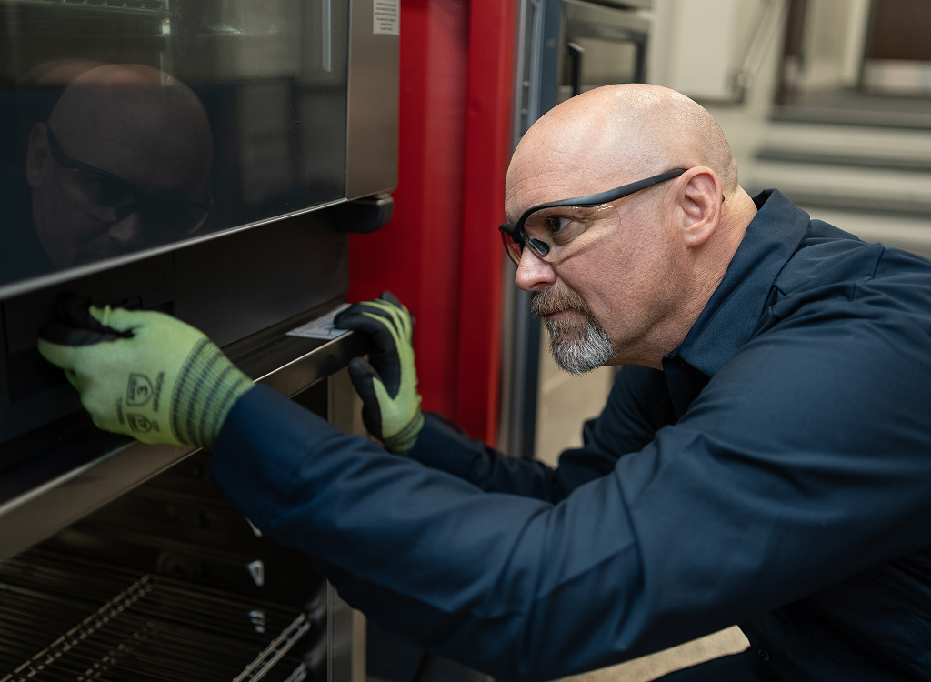 Technician in work gloves checking the door hinge of a commercial oven