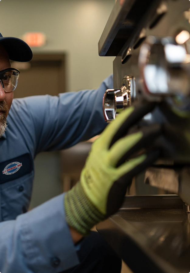 A-1 Services Group technician in safety glasses and work gloves repairing commercial kitchen equipment