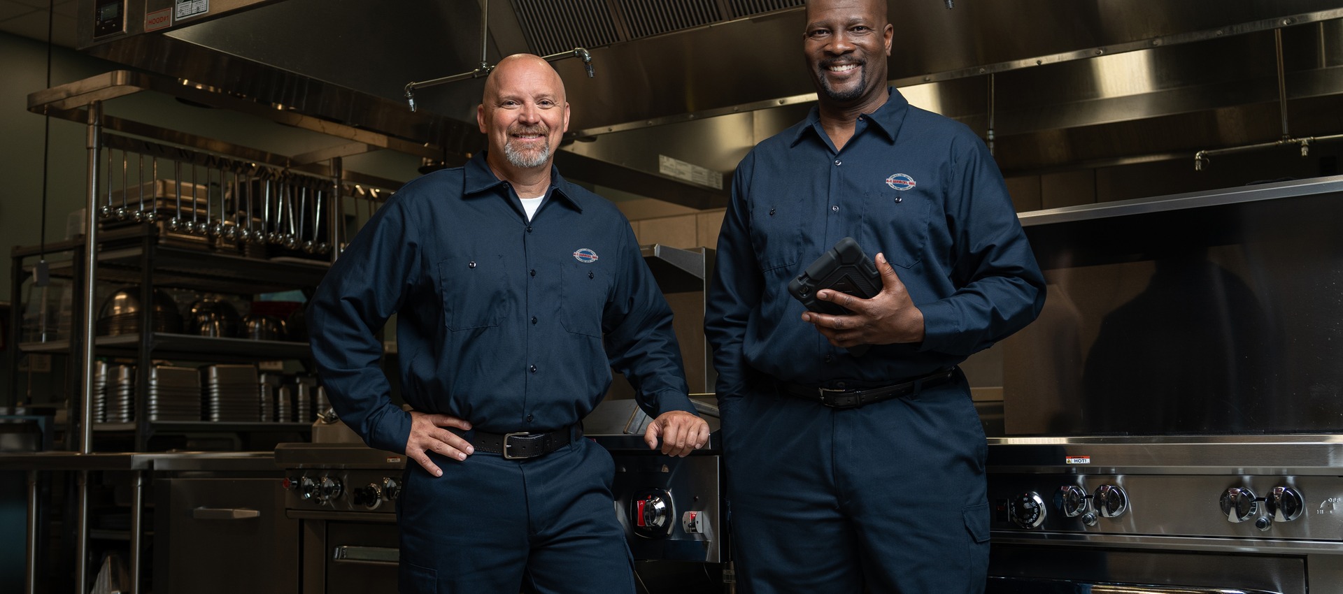 Two uniformed A-1 Services Group technicians standing side by side in a restaurant kitchen