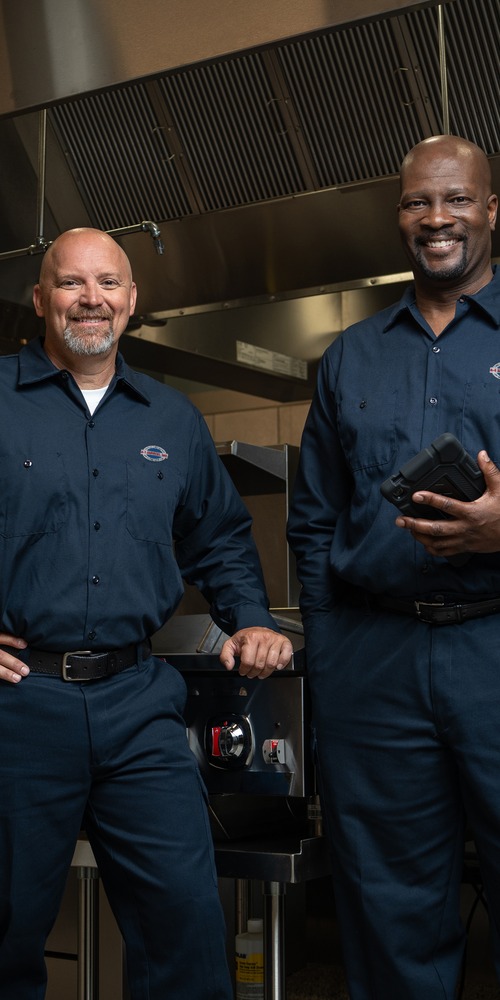 Two uniformed A-1 Services Group technicians standing side by side in a restaurant kitchen
