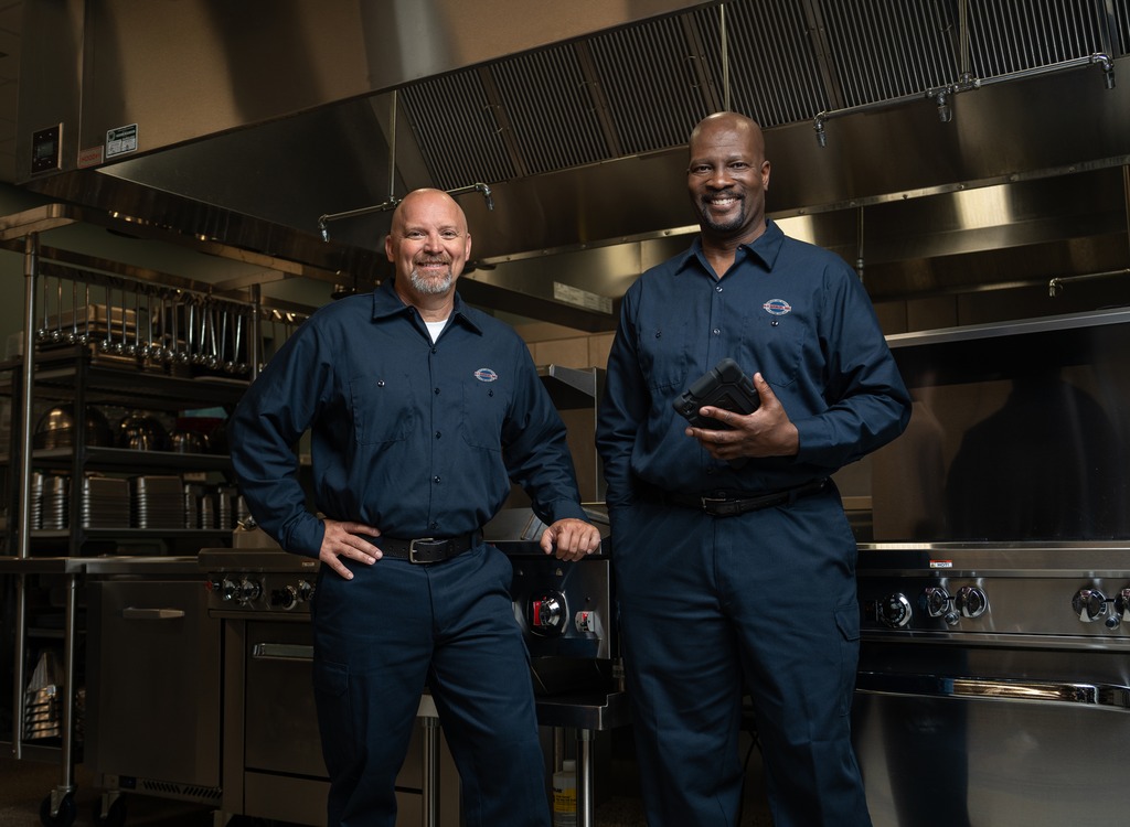 Two uniformed A-1 Services Group technicians standing side by side in a restaurant kitchen